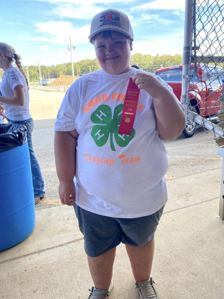 A smiling 4-H'er holds up a red second place ribbon