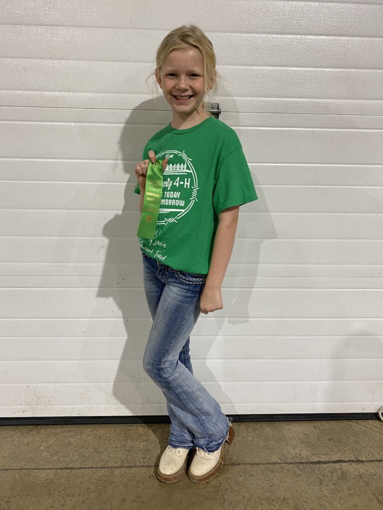A female 4-H'er grins and holds a up a green ribbon