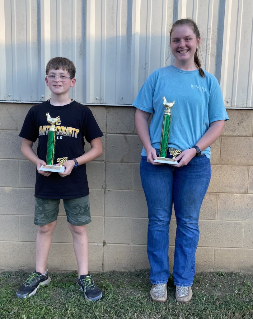 Two 4-H'ers smile while holding Chick Chain trophies