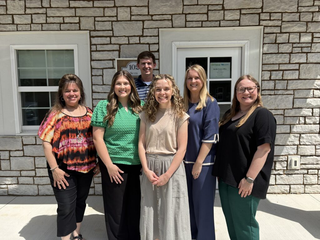 A group of 5 women and one man standing in front of an office building.